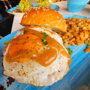 Double Smash Burger with pineapple bacon jam, sunny side up egg, house potato hash, and adobo gravy.